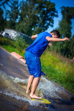 Yazın sığ sularda kaykay yapan genç bir adam aktif yaşam tarzının ve güneşli havanın tadını çıkarıyor. Açık hava aşırı su sporları aktivitesi.