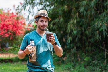 Sakallı, şapkalı ve yeşil gömlekli neşeli bir adam açık hava avlusunda hizmet ediyor. Gülümseyen bir keyif ifadesi. Arjantin ve Uruguay 'ın tipik yerba dostuyla sıcak bir içecek.,