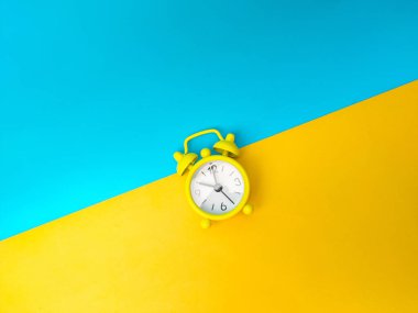 Top view yellow alarm clock on a yellow and blue background.