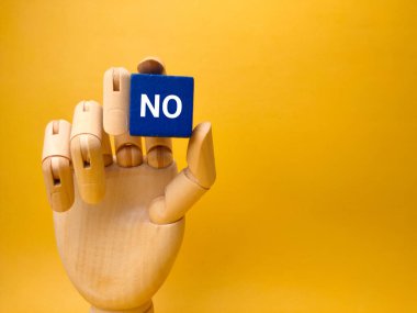 Wooden hand holding blue cube with the word NO on yellow background. Business concept.