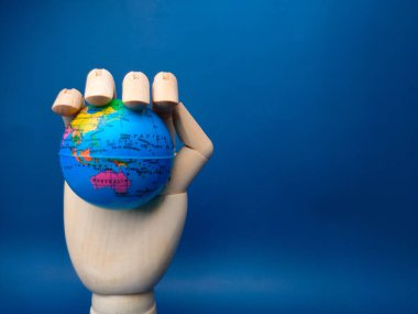 Wooden hand holding earth globe on a blue background.