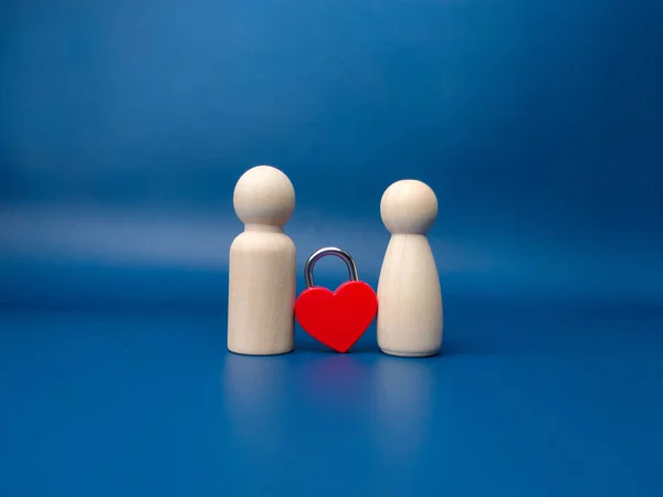 Couple of wooden peg doll with red love padlock on a blue background.