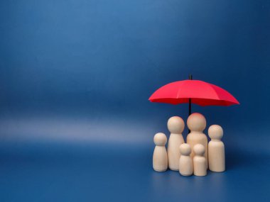 A family of wooden dolls are hiding under a red umbrella, protecting wooden peg dolls, planning, saving families, preventing risks and crises, health care and insurance concepts.