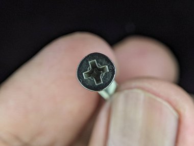Closeup finger holding stainless steel screw on a black background.