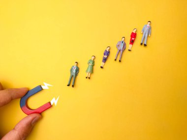 Hand holding magnet to attracts businessman on a yellow background.Business and leadership concept.
