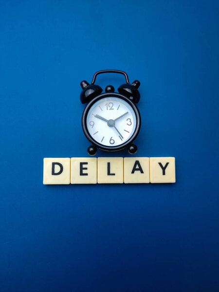 Black alarm clock with the word DELAY on blue background.