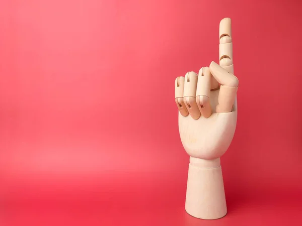 Wooden hand that is showing a one finger gesture on a red background with copy space.