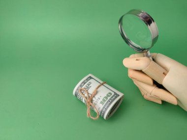 Tahta el, yeşil arka planda banknotları olan büyüteç tutuyor..