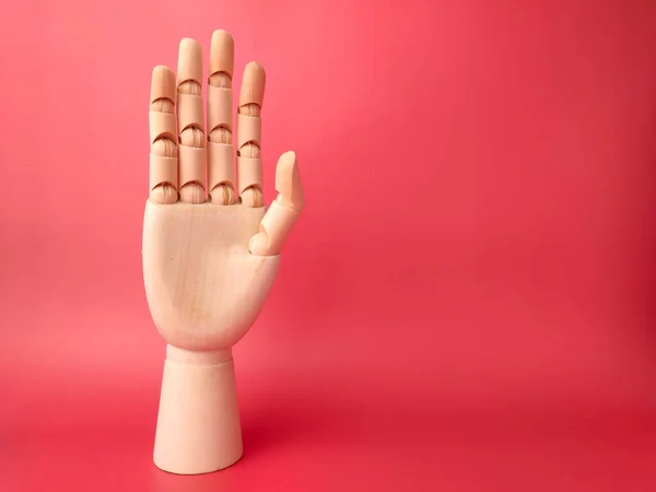 Wooden hand that is showing the style of raising hands on a red background.