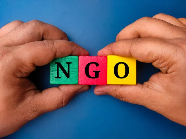 stock image Hand holding colored cube with the word NGO on blue background