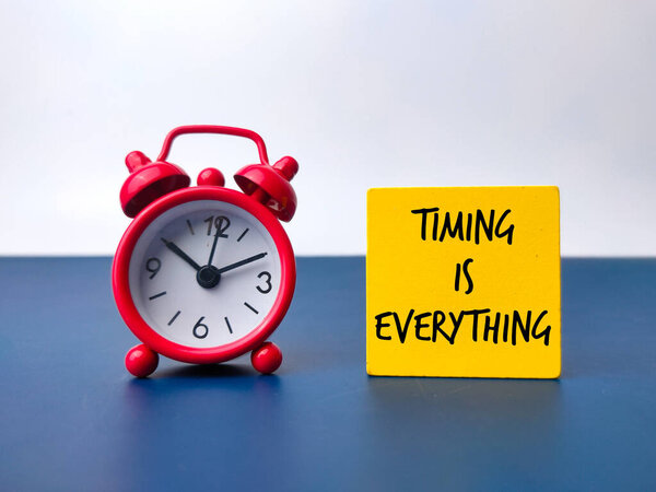 Красный будильник и цветной деревянный куб со словом TIMING IS EVERYTHING. Концепция бизнеса.