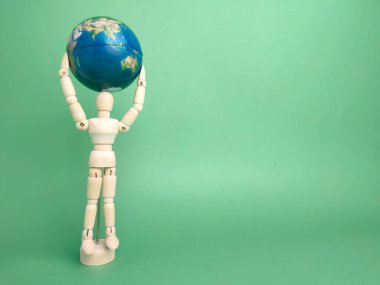 Yerküresini tutan tahta manken, fotokopi alanı olan yeşil bir arka planda..