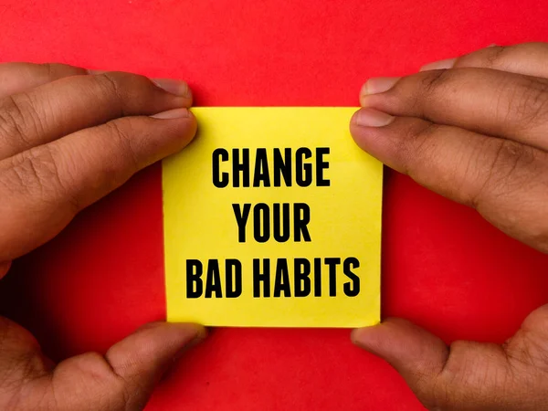 stock image Hand holding sticky notepaper with text CHANGE YOUR BAD HABITS on a red background. Business concept.