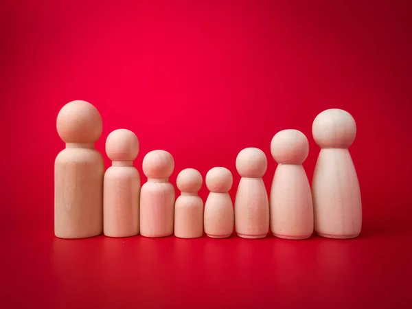 Wooden figures big family lined up according to their respective heights on red background.