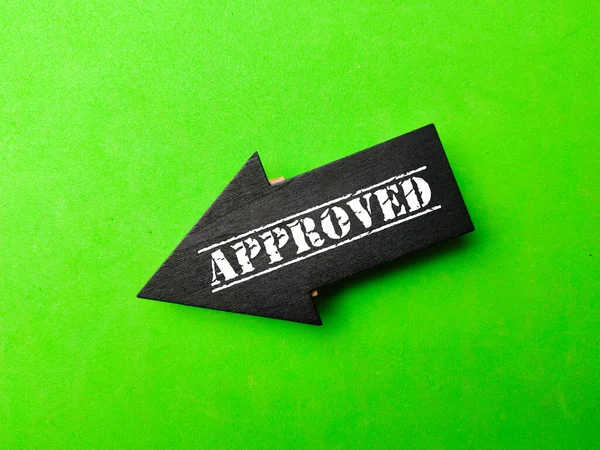 Wooden black arrow with the word APPROVED on a green background. Business concept.
