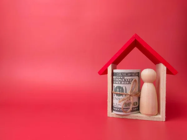 Wooden doll figures,banknotes and toy house on a red background with copy space.
