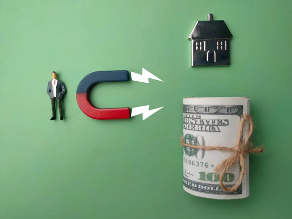 Miniature people with magnet attract house and banknote. The concept of buying a home