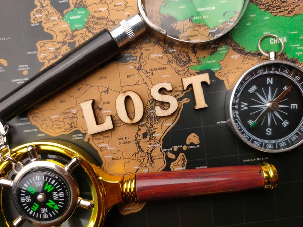 Magnifying glass,compass with the wooden word LOST on a world map background.