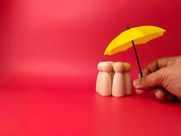 木製の人形のグループは 赤い背景に誰かが保持黄色の傘の下に隠れている — ストック写真
