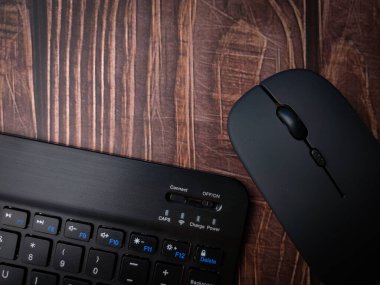 Malezya, 30 Nisan 2022: Kara Bluetooth kablosuz klavye ve tahta arka planda kablosuz fare.