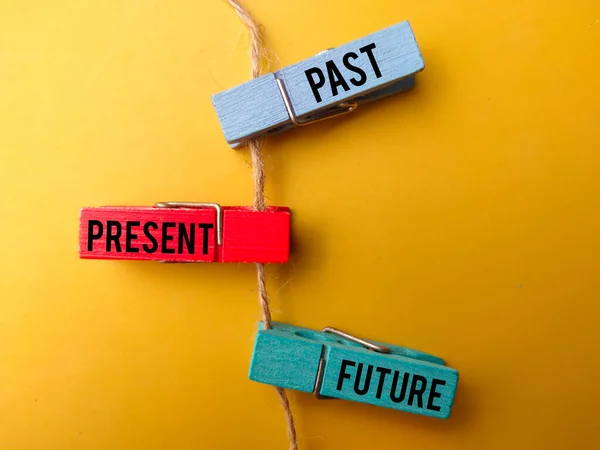 Colored wooden clips and roots with the word PAST PRESENT FUTURE on yellow background