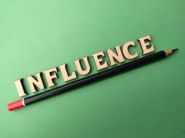 Tahta kelime ve kalem yeşil arka planda INFLUENCE sözcüğüyle