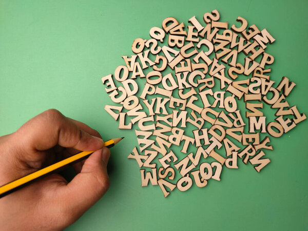 Someone hand holding pencil and with wooden word on a green background