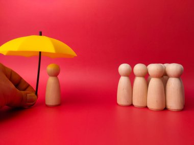 Bir grup ahşap heykel kırmızı arka plandaki birinin tuttuğu sarı şemsiyenin altına sığınmak için sıraya giriyorlar.