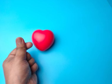 Kırmızı kalp şekli, mavi arka planda birinin elinden çıkan küçük bir aşk. Kalp kontrolü ya da aşk konsepti için kullanılabilir