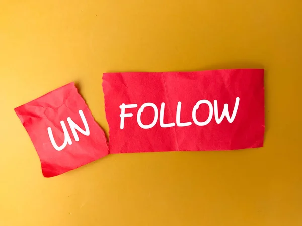 Cutting red paper with the word UNFOLLOW on a yellow background