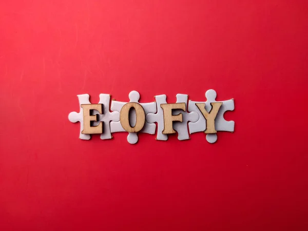 stock image Top view wooden word and white puzzle with the word EOFY on a red background