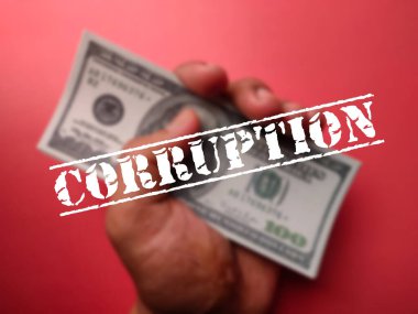 Birisi elinde kırmızı arka planda CORRUPTION sözcüğüyle banknotlar tutuyor.