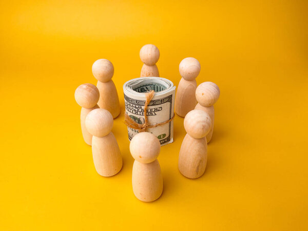 Money surrounded by wooden peg doll on a yellow background. Crowdfunding concept.