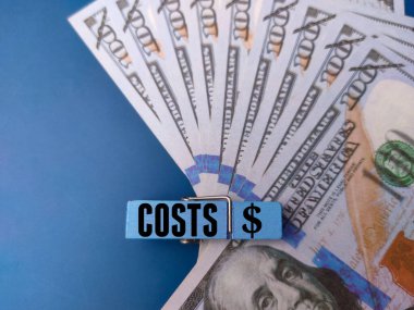 Banknotlar ve ahşap klipler mavi arka planda COSTS sözcüğüyle