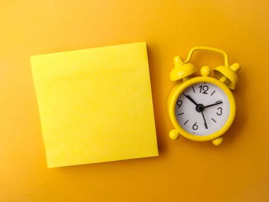Sarı zemin üzerinde alarm saati olan yakın plan sarı yapışkan nota kopyalama alanı ile.