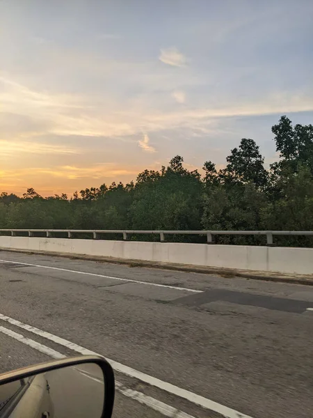View sunset and mangrove swamp trees along the road from inside a vehicle.