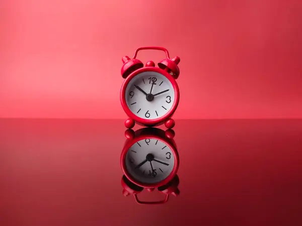 Red alarm clock with reflection on a red background