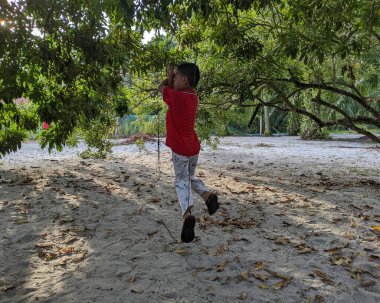 Perak, Malezya, 30 Temmuz 2023: Bir çocuk bir gol attıktan sonra ünlü futbolcu stili yaparken bir ağacın altında futbol oynuyor.