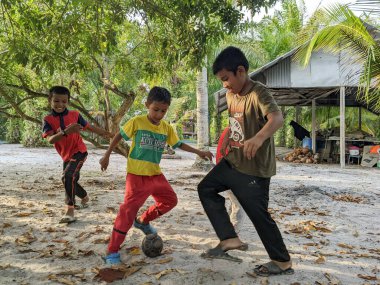 Perak, Malezya, 30 Temmuz 2023: Bir çocuk akşam bahçelerinde bir ağacın altında futbol oynuyor.
