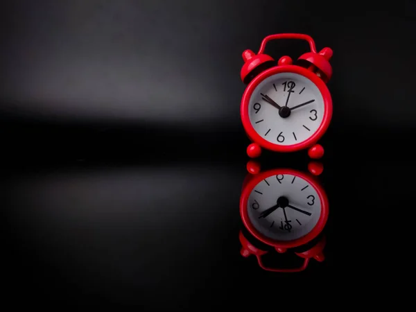 Red alarm clock on black background with reflection on a black acrylic board. Copy and text space.