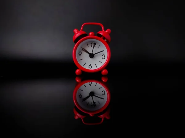 Red alarm clock on black background with reflection on a black acrylic board