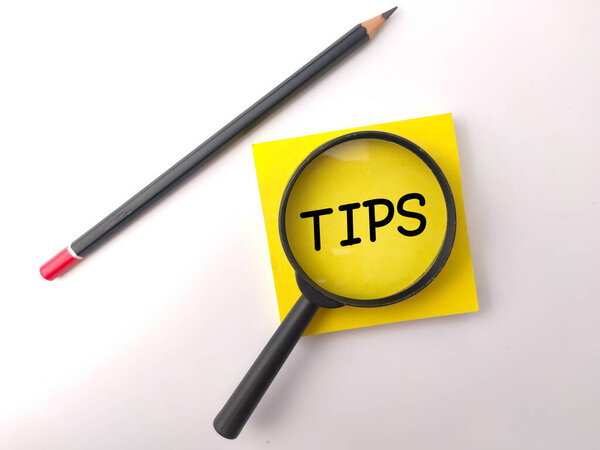 Word Tips writting on sticky note with pencil and magnifying glass on a white background