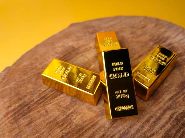 Sarı arka planda ahşap ve finansal konsepti ve kavramsal imajı olan altın külçeler