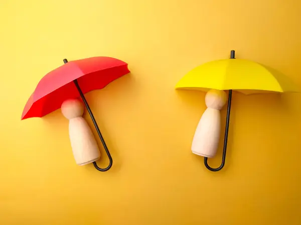 Wooden figures covered by umbrella on a yellow background. Personal insurance concept.