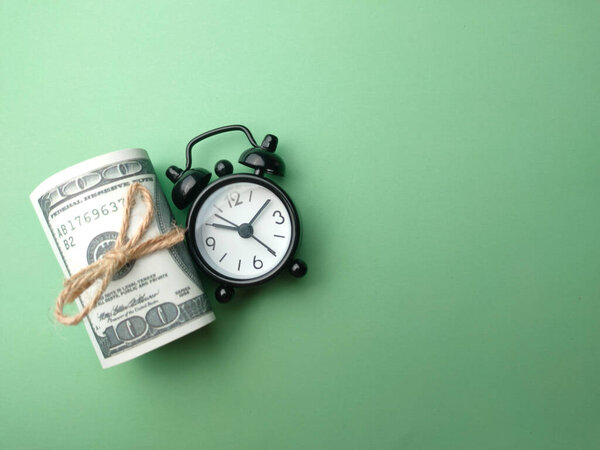 Top view alarm clock and banknotes on a green background with copy space.