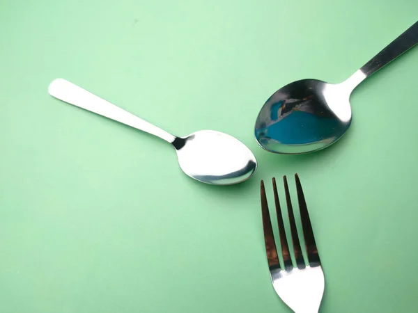 Spoons, forks and teaspoons arranged on a green background.