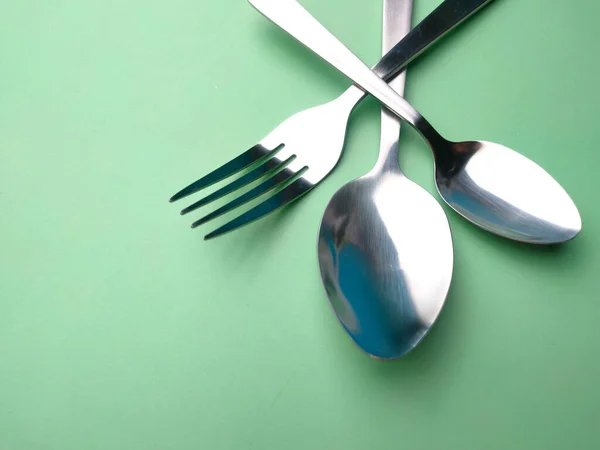 Spoons, forks and teaspoons arranged on a green background.