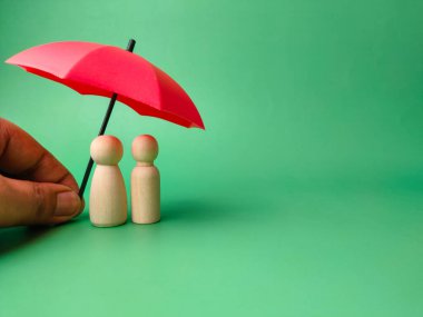 Kırmızı şemsiyeli biri yeşil arka plandaki tahta bebekleri korur.