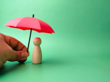 Birisi elinde kırmızı şemsiyeyle yeşil arka plandaki tahta bebeği koruyacak..