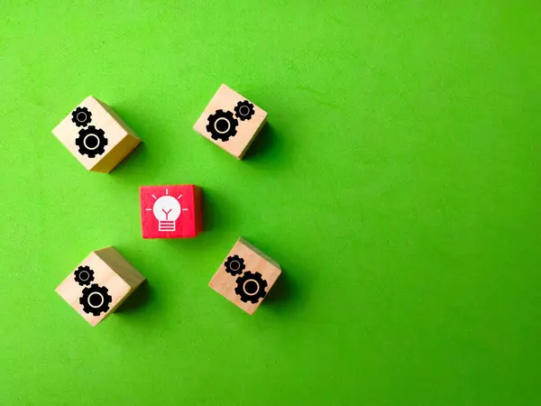 Wooden blocks with cogwheel and light bulb symbols on a green background.